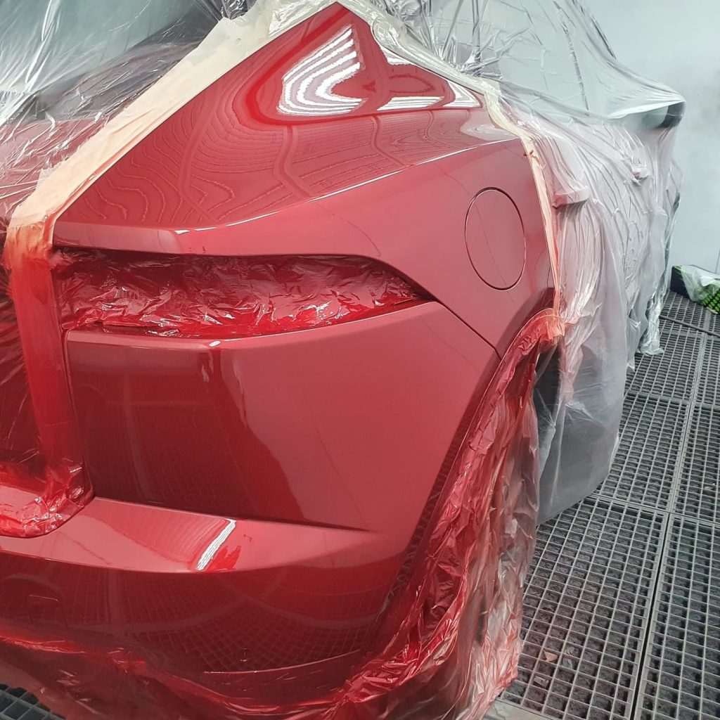 Close-up of rear light cluster and bumper of red car during spray painting.